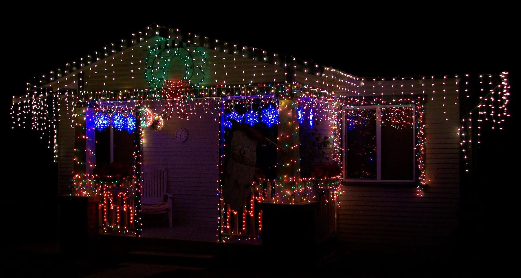 House covered in multicolor Christmas lights on the roofline and porch